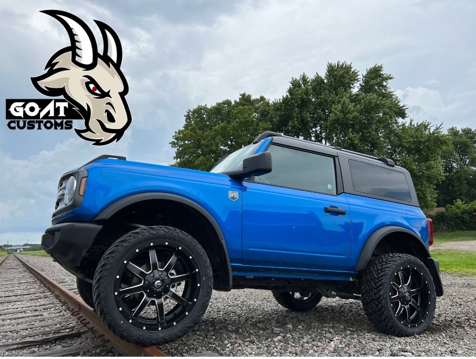 Blue 2-door Ford Bronco with lift kit and black wheels parked by railroad tracks