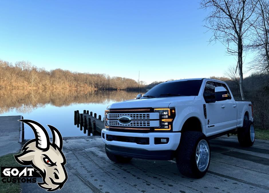 White lifted Ford Super Duty parked at a lakeside boat launch at dusk