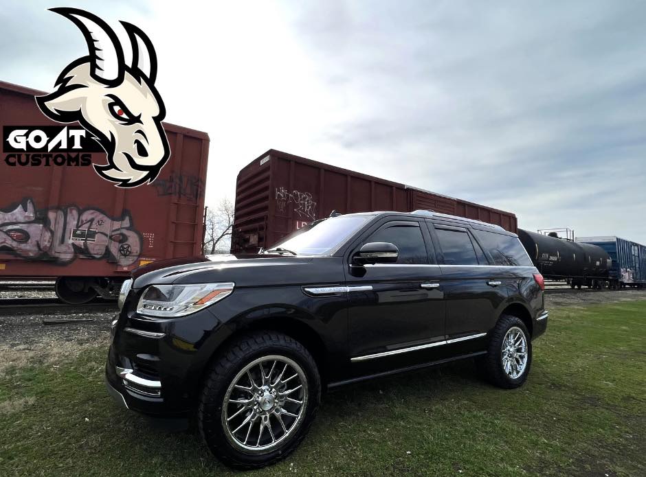 Black Lincoln Navigator with custom wheels parked in a rail yard